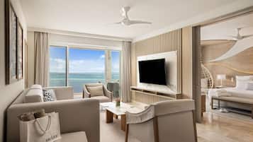 Quarto de hotel moderno com televisão grande, assentos confortáveis, vista para o mar e ventoinha de teto.