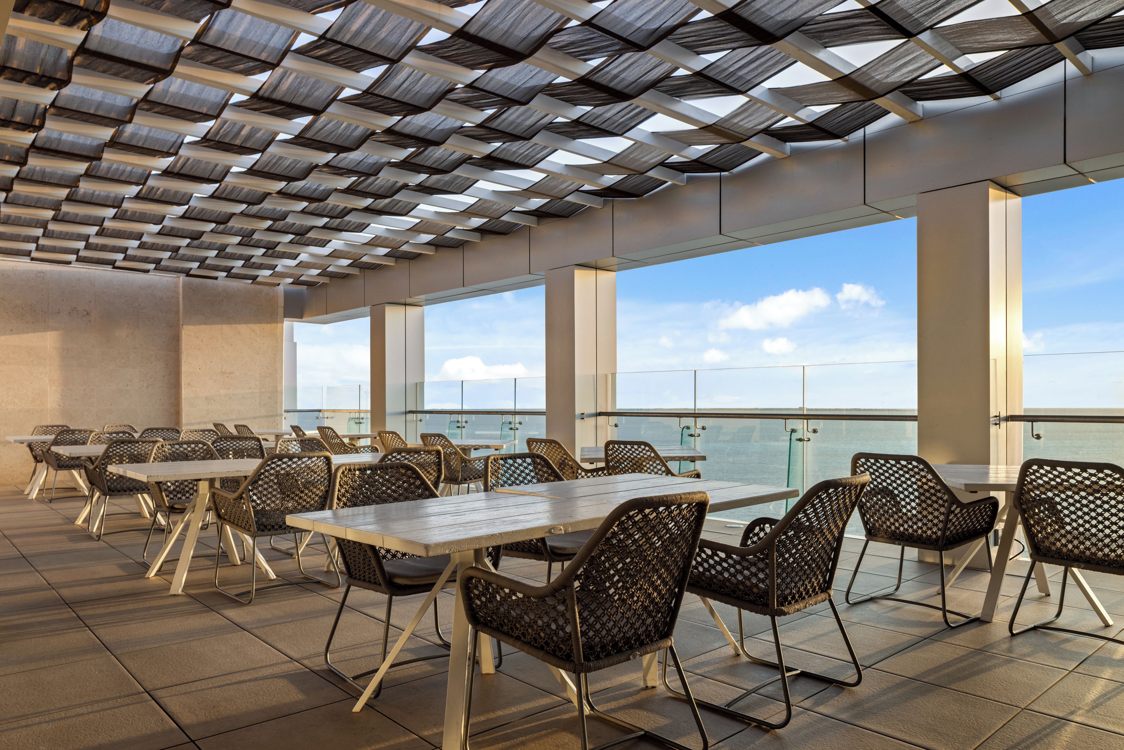 Un espace extérieur aménagé pour les repas, avec des tables et des chaises, de grandes fenêtres et une vue sur le ciel.