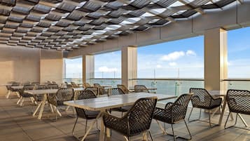Un espace extérieur aménagé pour les repas, avec des tables et des chaises, de grandes fenêtres et une vue sur le ciel.