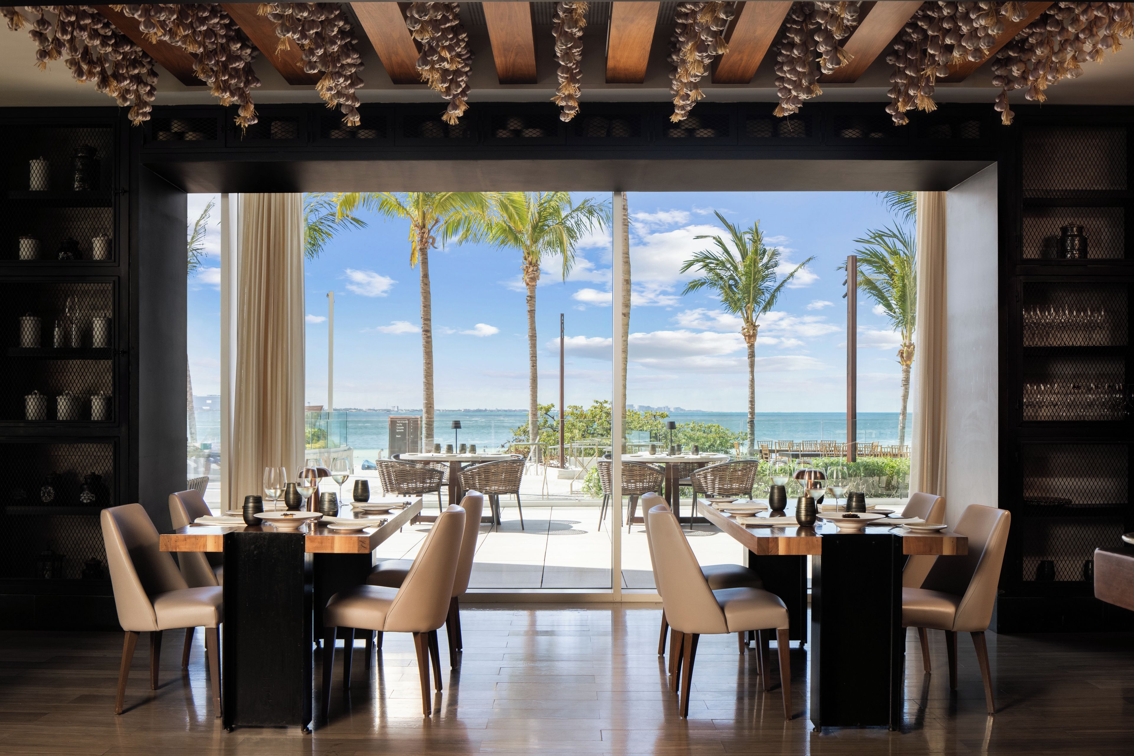 A dining area with a view of the ocean, featuring a table set for four, chairs, and a large window.