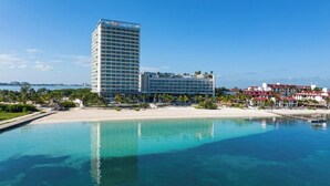 A hotel with a large building, a beach, and a pool.