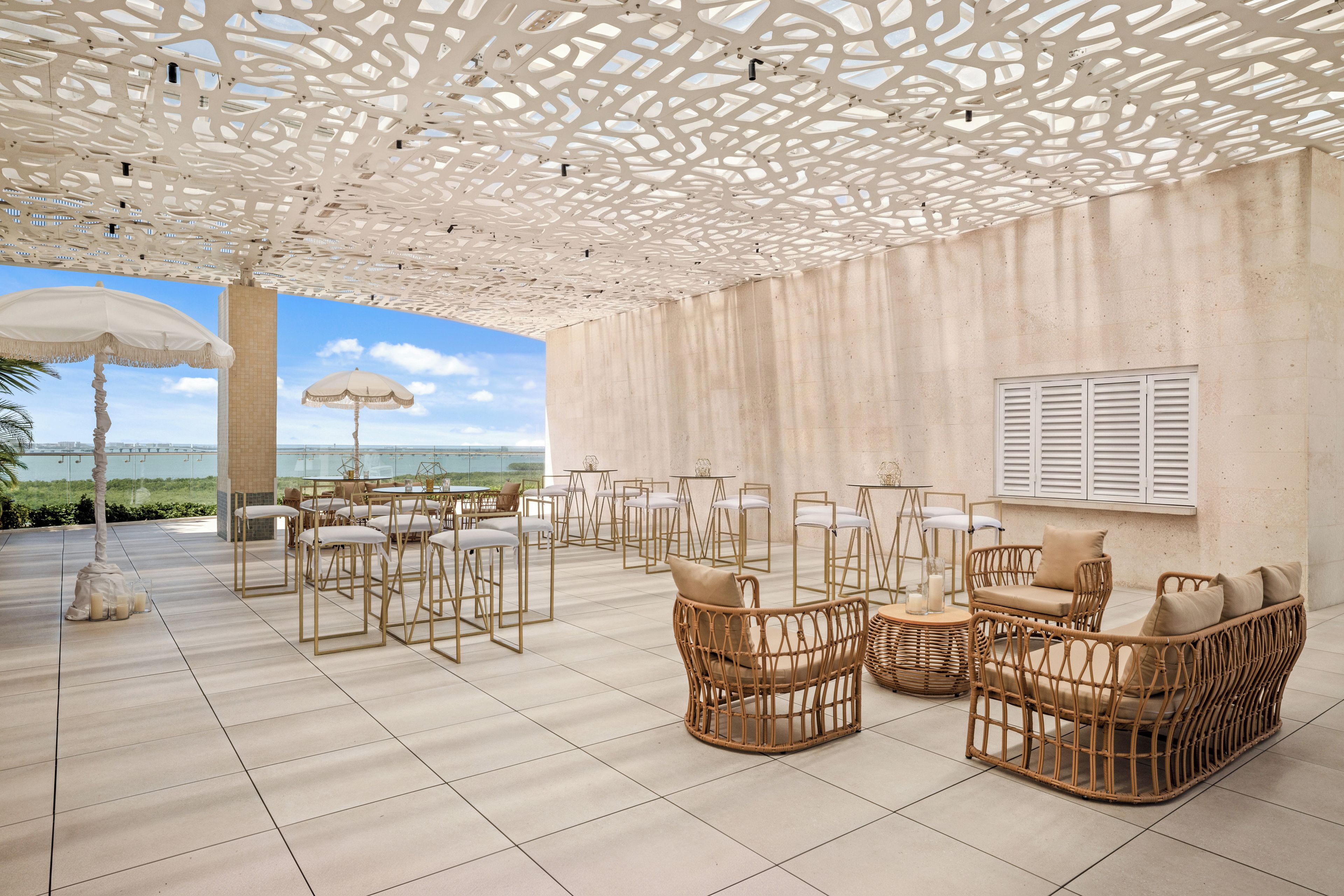 An outdoor seating area with wicker furniture, a patterned ceiling, and a view of the sea.