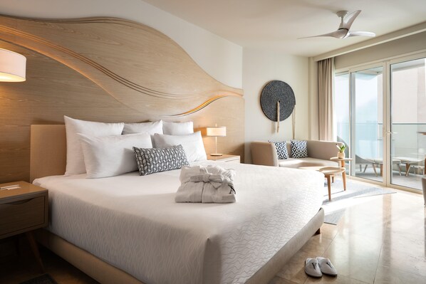 Habitación de hotel con una cama grande, ventilador de techo, vista de la ciudad y balcón con asientos.