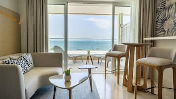 Una habitación de hotel moderna con sofá, dos sillones, una mesita y vista al mar.