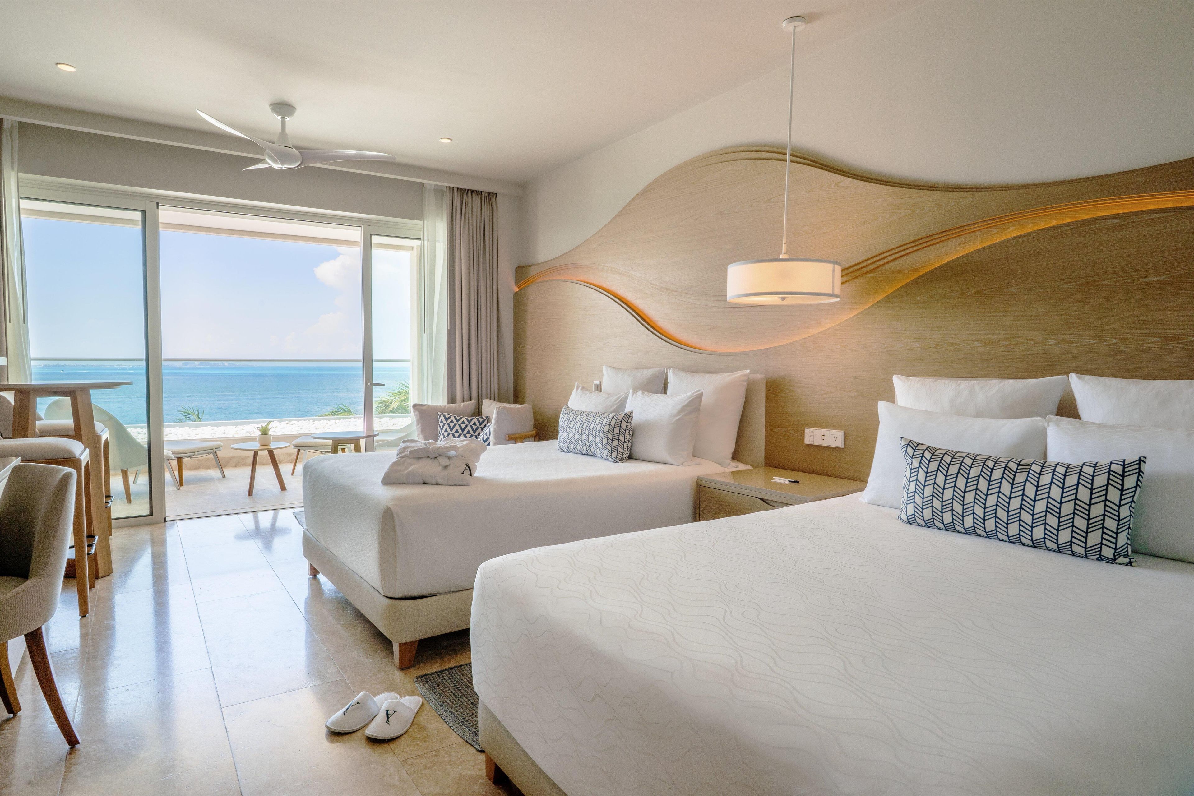 Habitación de hotel con dos camas, vista al mar y zona de comedor con mesa y sillas.