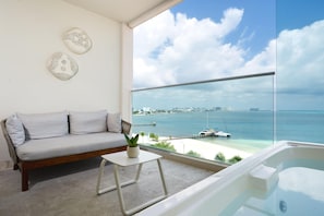 Uma varanda com sofá, uma mesa pequena com planta e vista para o mar e o horizonte da cidade.