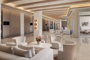 Un hall d’entrée spacieux au design moderne, comprenant un comptoir d’accueil, un espace salon et une grande fenêtre offrant une vue sur l’extérieur.