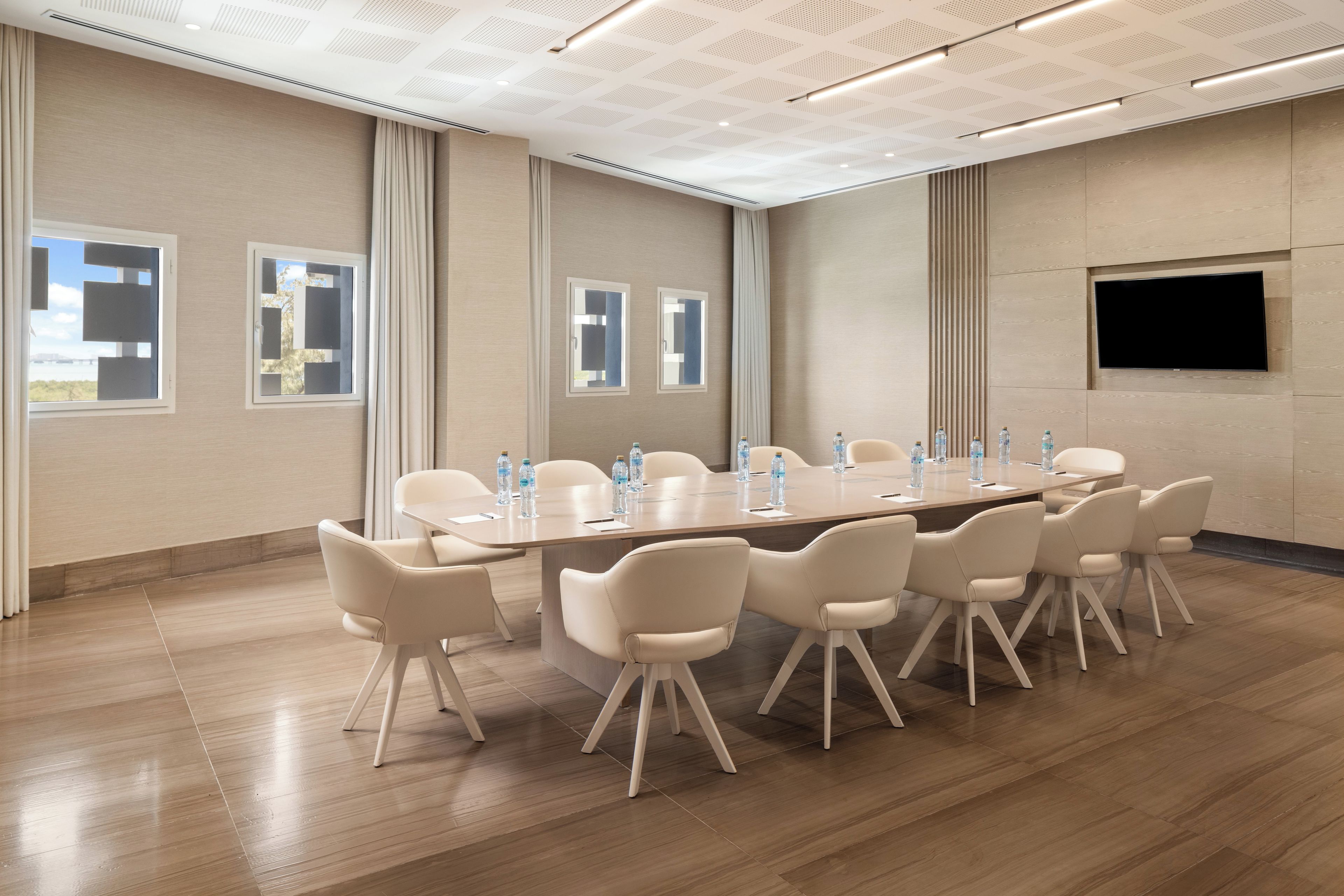 Un salón de conferencias con una mesa larga, varias sillas y botellas de agua.