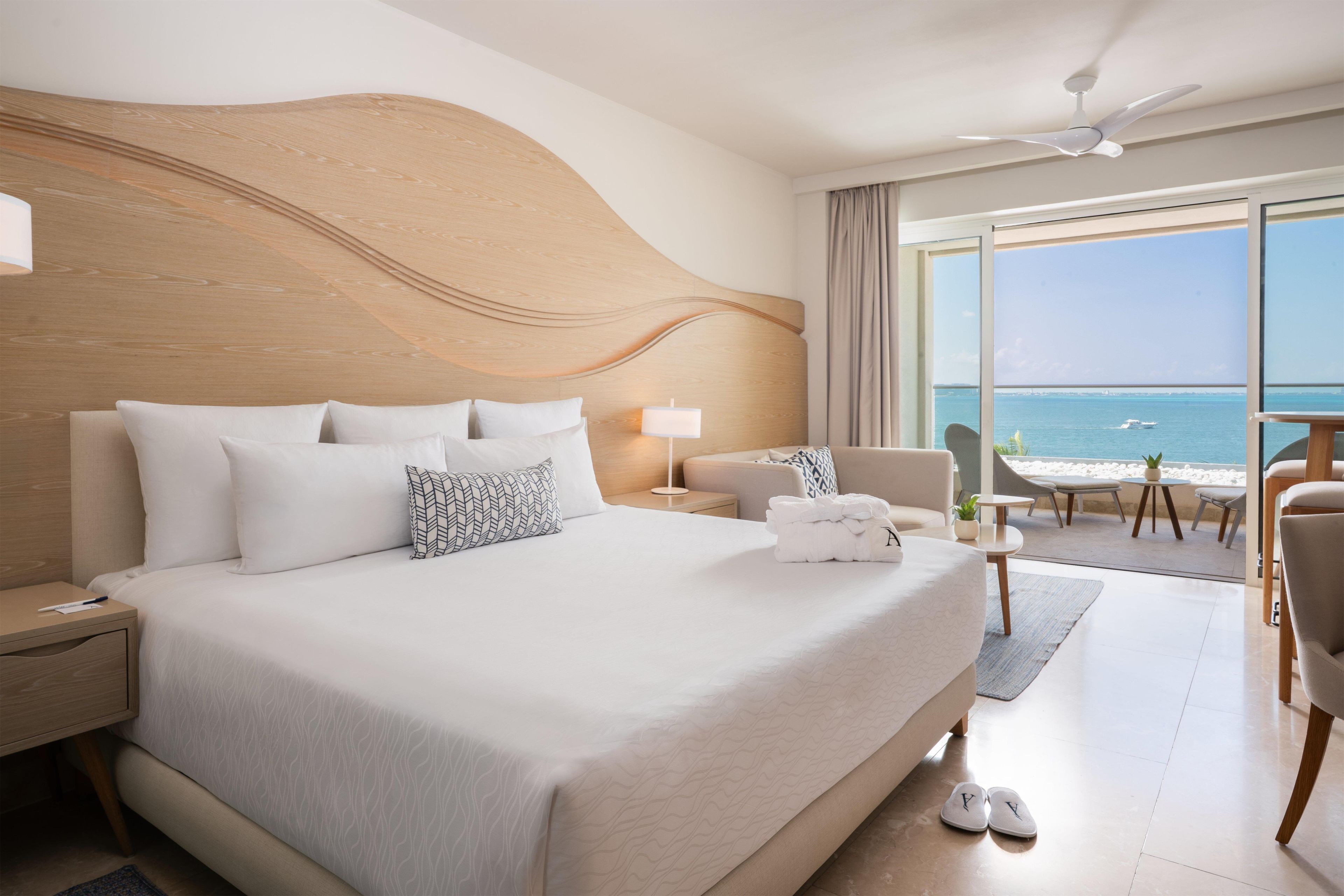Habitación de hotel con una cama grande, un escritorio, una silla, un balcón con vistas al mar y un ventilador de techo.