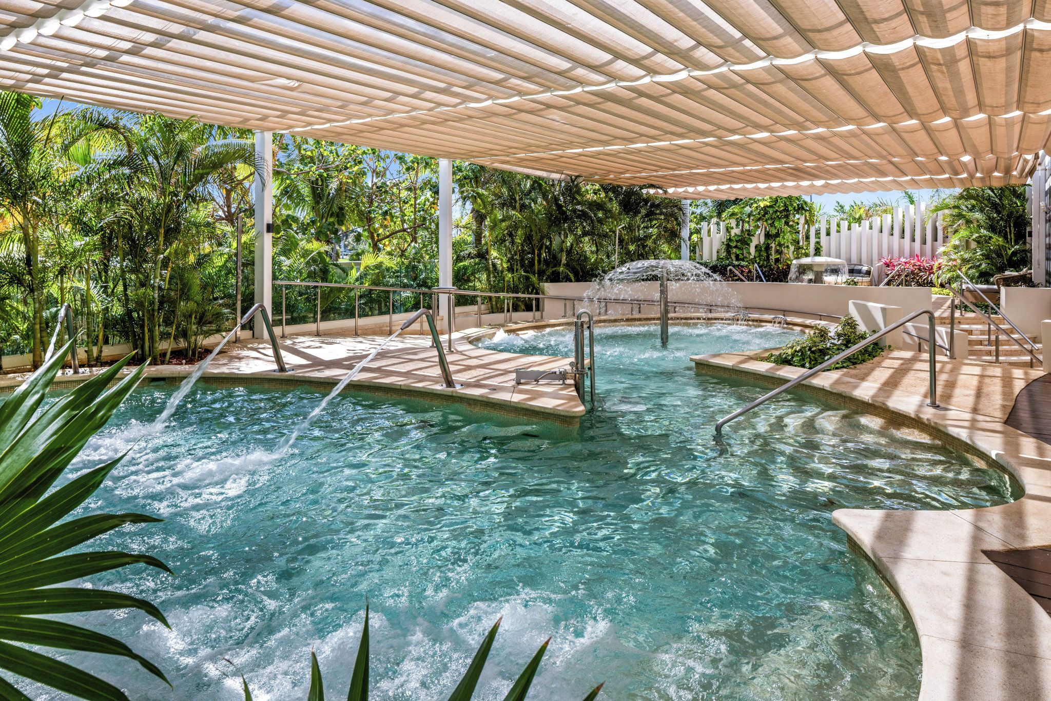 A pool area with a canopy, steps leading into the water, and surrounding greenery.