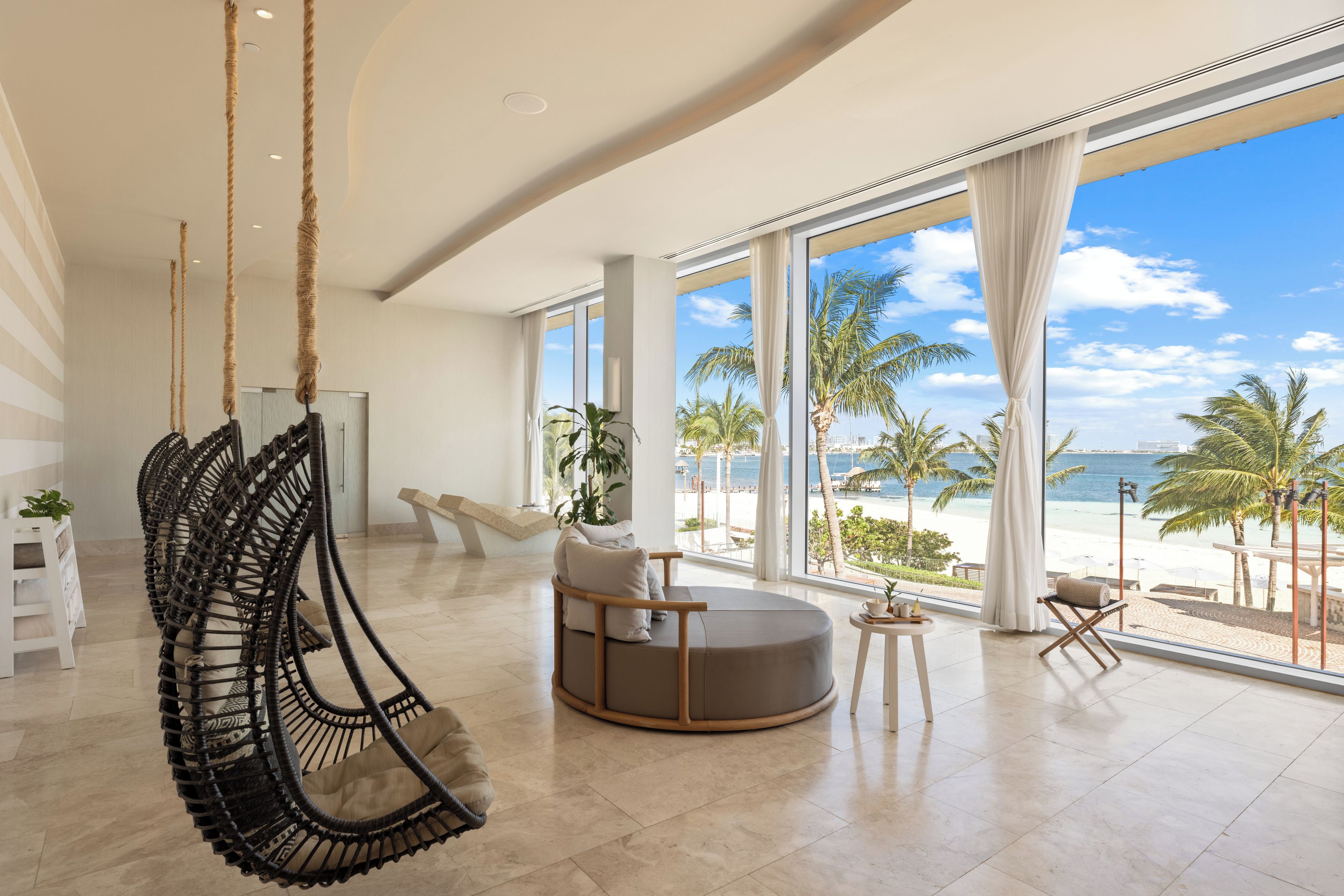 Quarto espaçoso com grande janela com vista para a praia, uma cadeira suspensa e um espaço de estar circular.