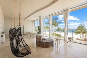 Une pièce spacieuse avec une grande fenêtre donnant sur une plage, un fauteuil suspendu et un espace salon circulaire.