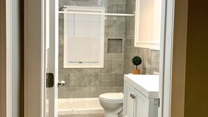 A modern bathroom with a bathtub, toilet, and vanity. - The Roulette Duplex-Private Yard&Parking (Niagara Falls)