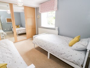 A bedroom with two single beds, a wardrobe, a window with a view, and a mirror. - 2 Cae Mattw (Abergele)