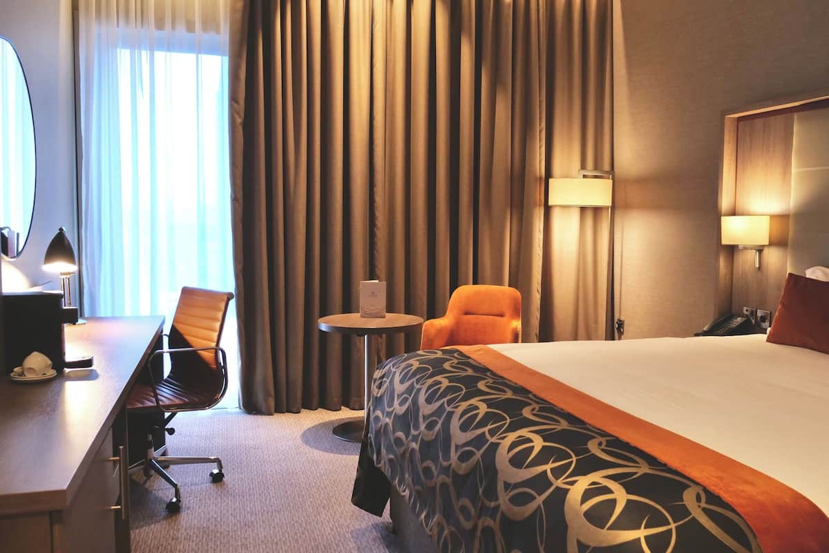 Une chambre d’hôtel avec un grand lit, un bureau avec une chaise, une petite table et une lampe.