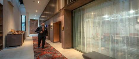 A modern hotel lobby with a long corridor, a reception desk, and a glass wall with a view.