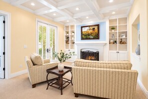 A living room with two sofas, a coffee table, and a fireplace. There are shelves with decorative items and a framed picture above the fireplace. - Private Pool & Outdoor Kitchen (Hurricane)