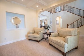 A living room with two armchairs, a small table, and a decorative mirror on the wall. A staircase with a railing is visible in the background. - Private Pool & Outdoor Kitchen (Hurricane)