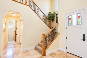 A hallway with a wooden staircase, a white door with stained glass, and a plant.