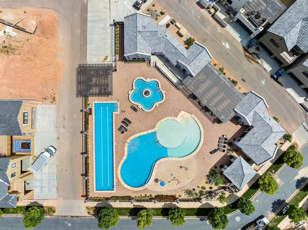 An aerial view of a residential area with a swimming pool, a tennis court, and houses with sloped roofs.