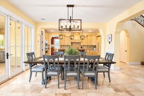 A spacious dining area with a large table and chairs, a chandelier, and a view into the kitchen.