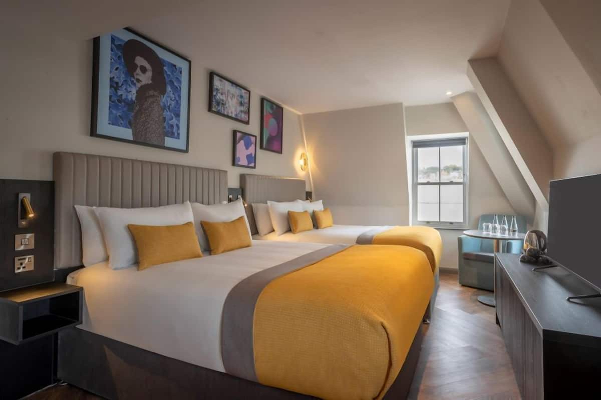 A hotel room with two beds, a TV, a desk, and artwork on the walls.