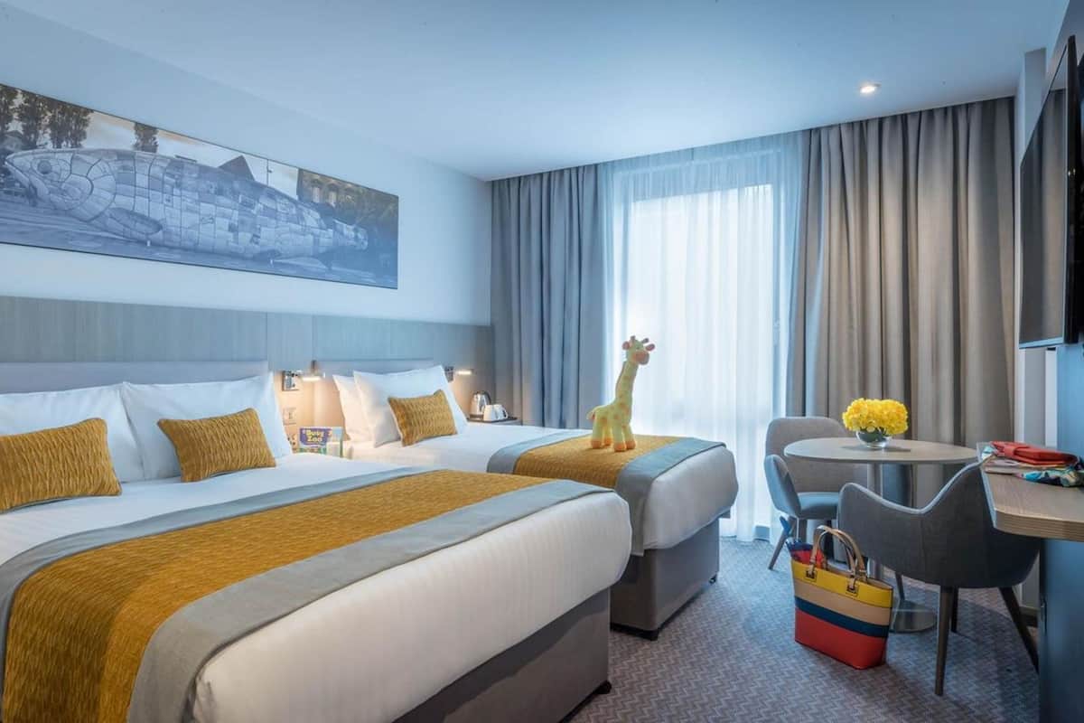 A hotel room with two beds, a desk, a chair, and a giraffe toy.