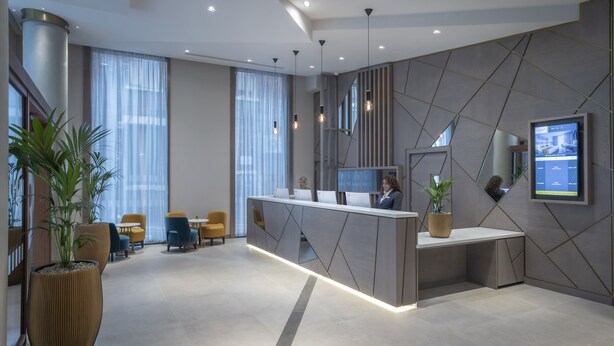 A modern reception area with a desk, chairs, and a large potted plant. - Maldron Hotel Manchester City Centre (Manchester)