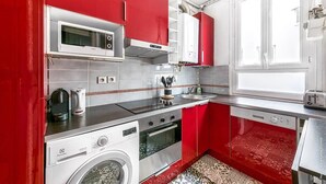 Cocina compacta con armarios rojos, microondas, estufa, lavadora y tostadora.