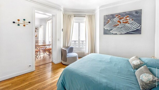 Un dormitorio con cama, una silla, un cuadro y vistas a un balcón.