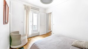 Un dormitorio con una cama, una silla y un ventanal con cortinas.