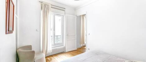 A bedroom with a bed, a chair, and a window with curtains.