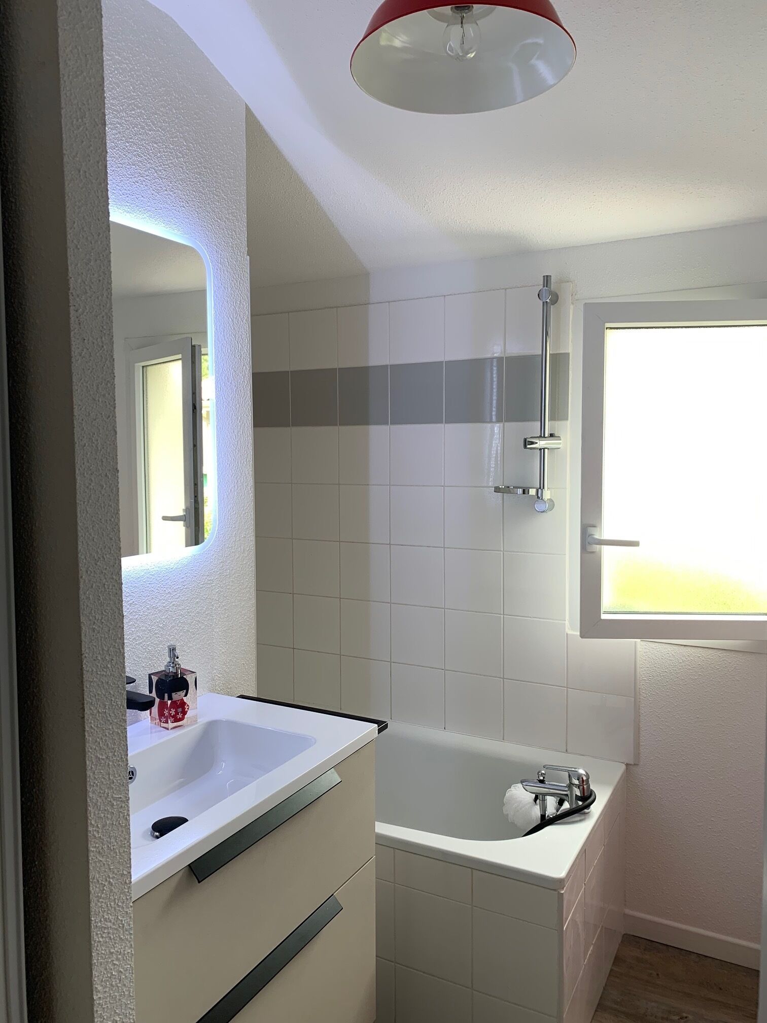 A bathroom with a white sink, a mirror, a shower, and a window.