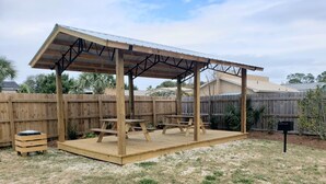 A wooden deck with picnic tables and a metal roof structure.