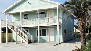 A two-story building with a balcony on the second floor, a visible address number, and a palm tree in the foreground.