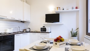 Una cocina moderna con armarios blancos, una estufa negra, un microondas y una mesa de comedor con platos, vasos y cubiertos.