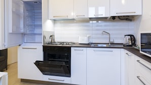 Una cocina moderna con gabinetes blancos, horno empotrado, estufa a gas, microondas y cafetera.