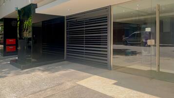 Fachada de edificio moderno con entrada de vidrio, una puerta metálica con persiana y suelo de hormigón.