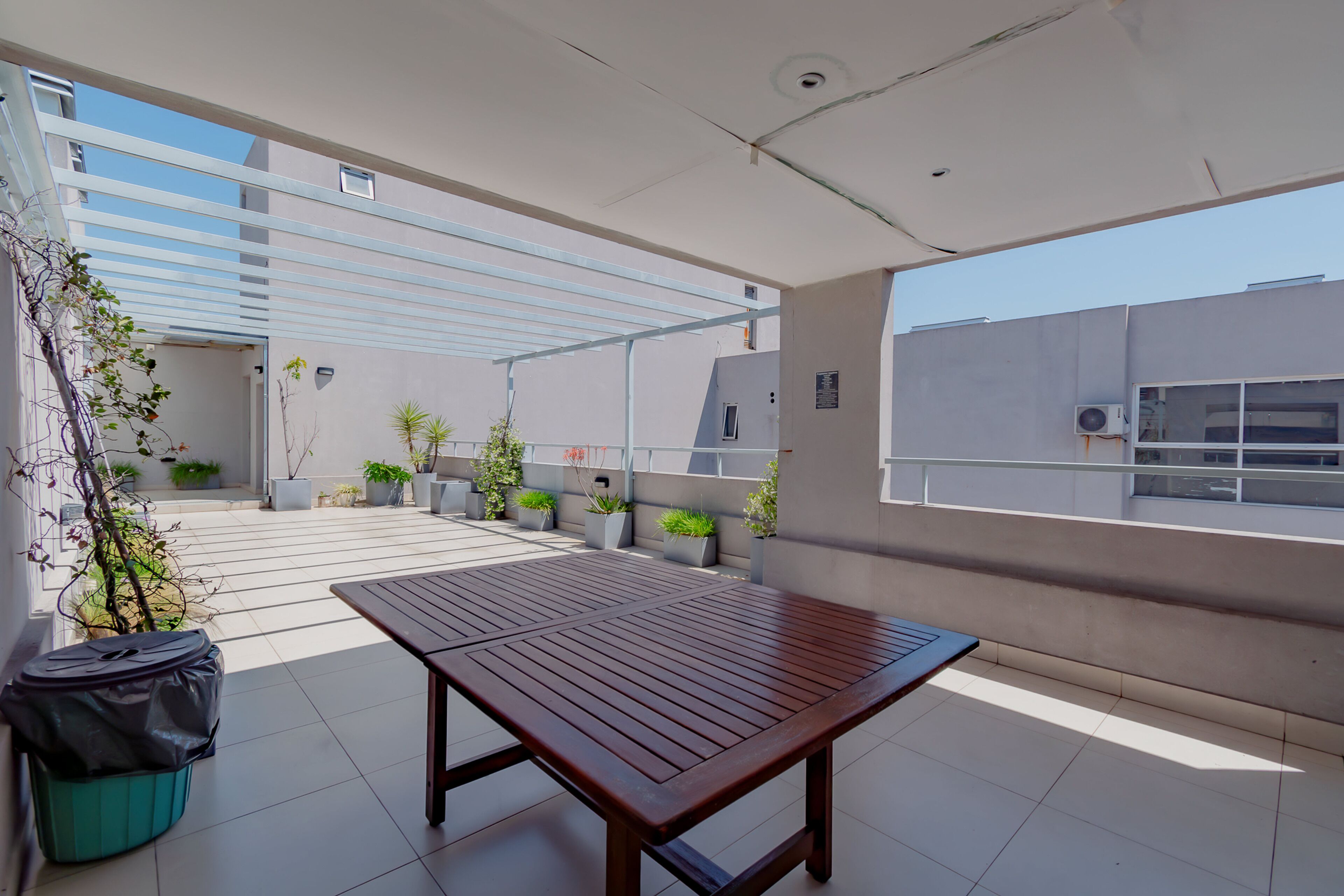 Una terraza en la azotea con una mesa de madera, plantas en macetas y vistas de la ciudad.