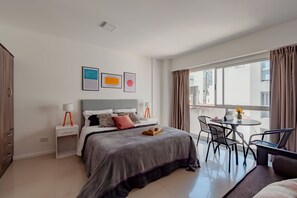 A modern hotel room with a large bed, a dining area with a table and chairs, and a view of the city through large windows. - BT Homes - Palermo, Gorriti (Buenos Aires)