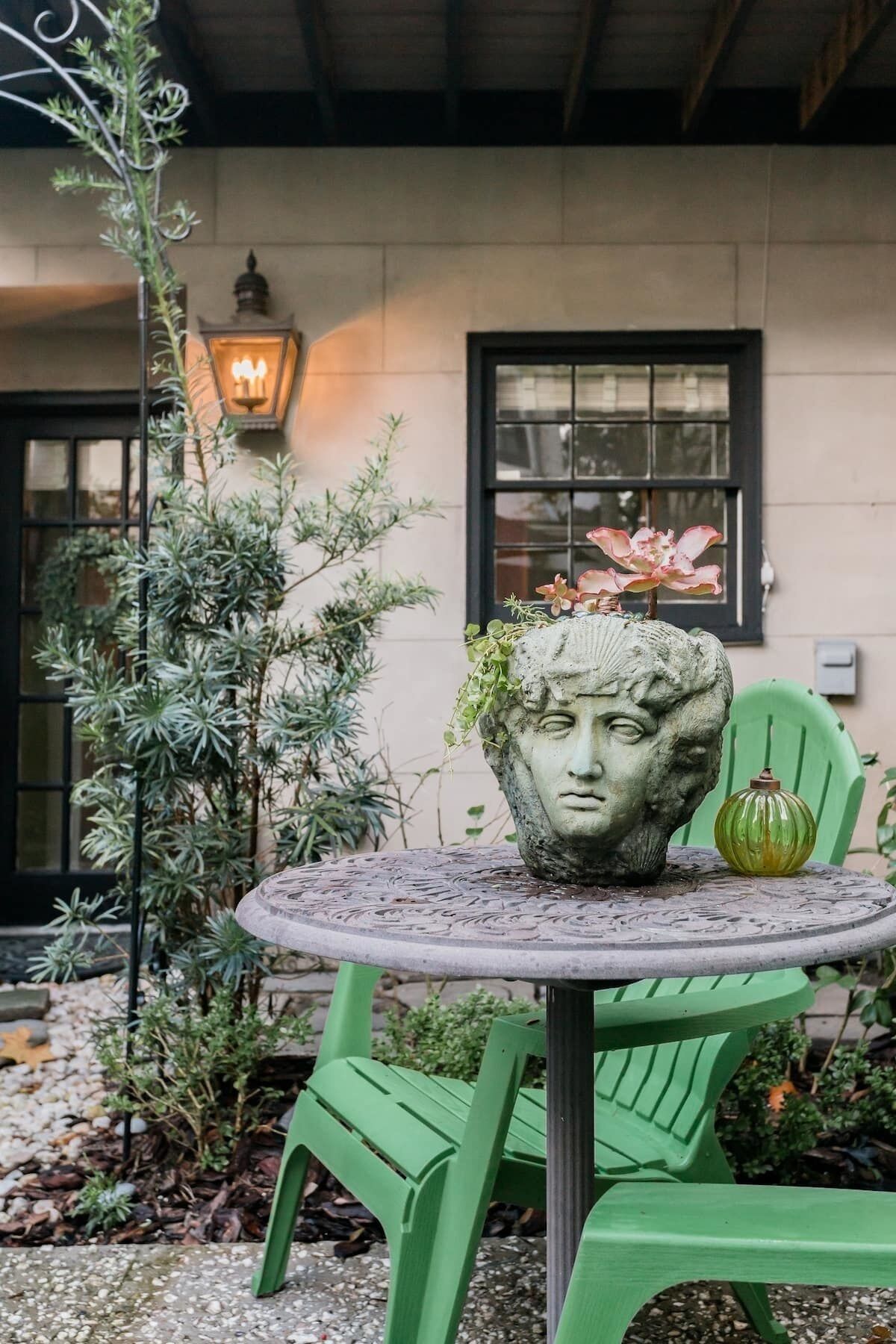 Una mesa redonda con una escultura decorativa en el cabecero, sillas verdes y una planta en maceta.