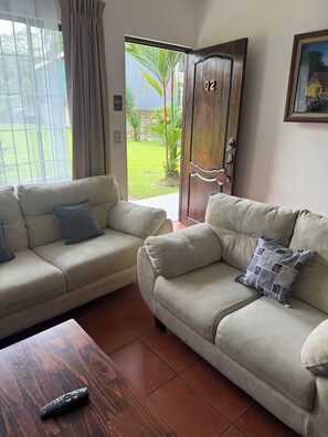 Ein Wohnzimmer mit zwei beigen Sofas, einem Holztisch und einer Tür, die nach draußen führt.
