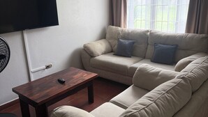 A living room with a sofa, a coffee table, a TV, and a window with curtains.