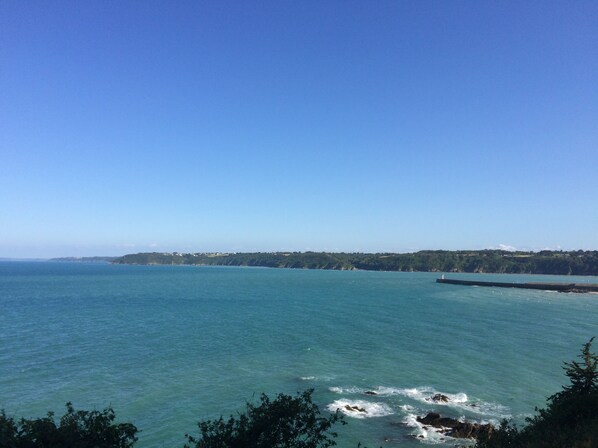 Vista costera con cielos despejados, mar tranquilo y una costa lejana con vegetación.