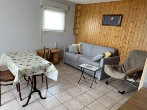 Una habitación con una mesa de comedor, un sofá gris, una pequeña mesita auxiliar y una pared de madera con un cuadro enmarcado.