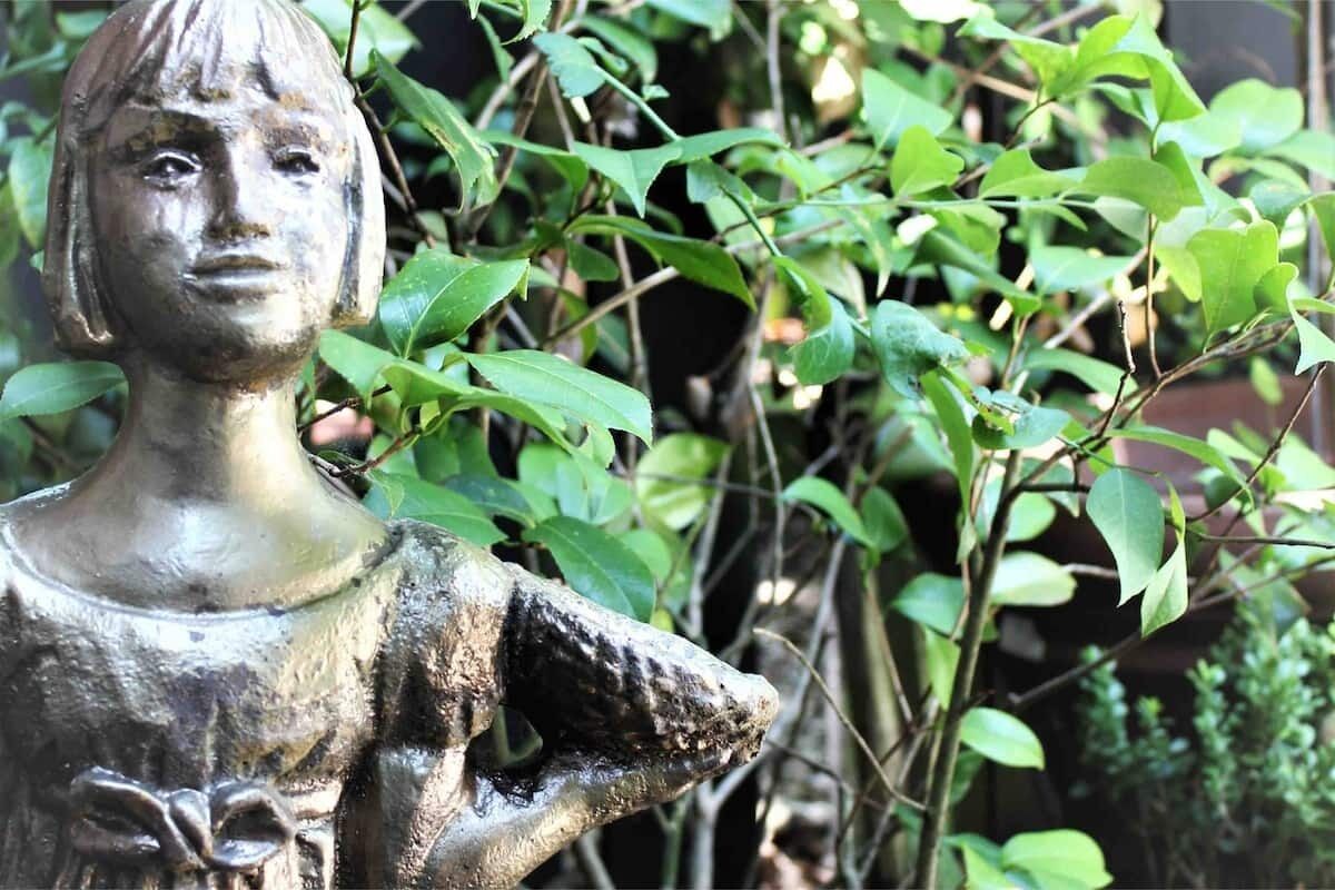 A sculpture of a person with a raised arm, surrounded by green foliage.