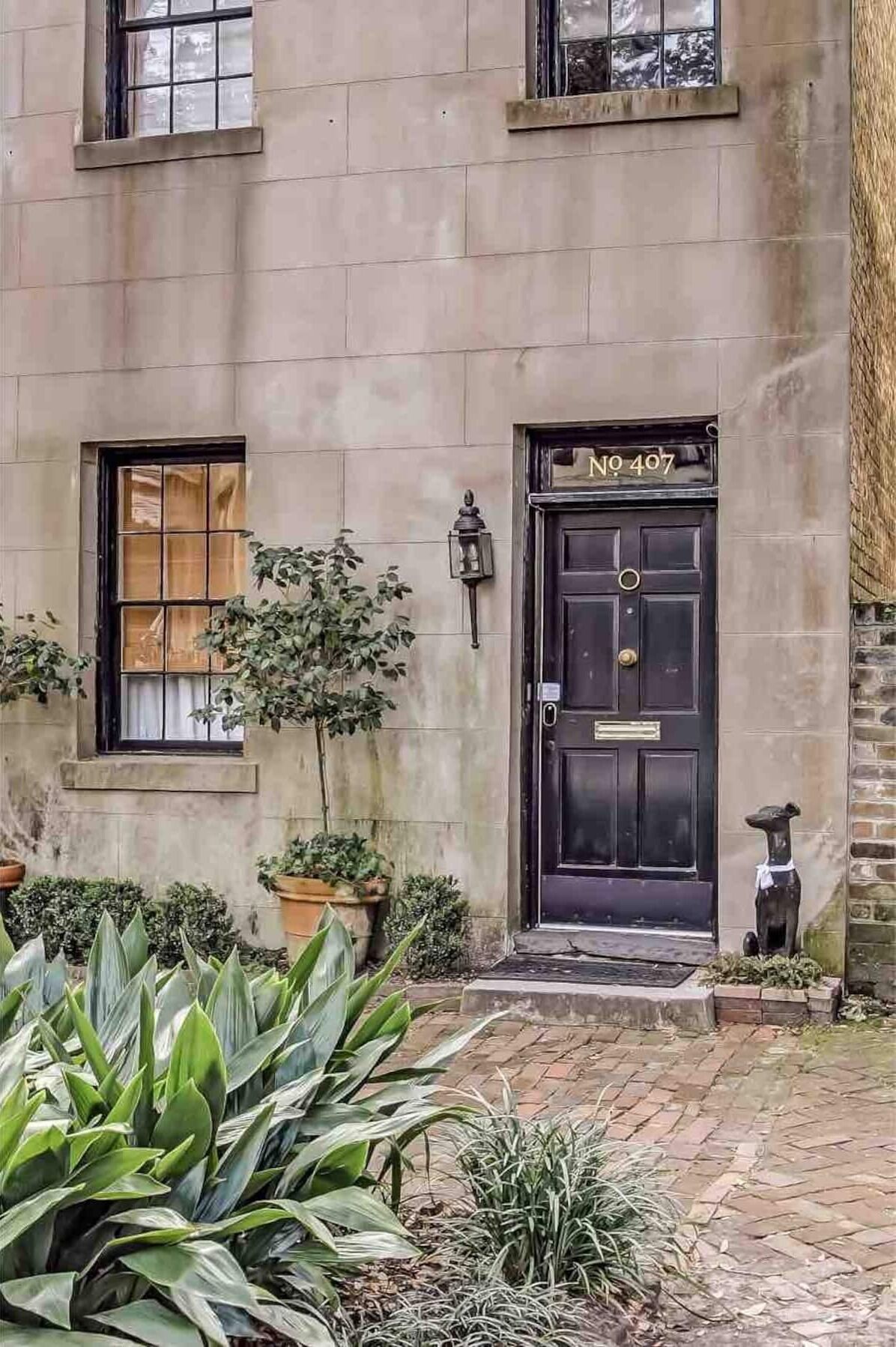 A building with a black door marked "No 407," a small window, and a potted plant in the foreground.