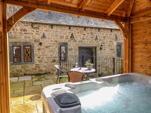A stone building with a wooden balcony, a hot tub, and outdoor seating. - Bluebell Cottage (Alfreton)