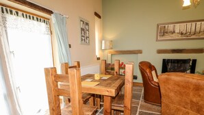 Ein gemütliches Wohnzimmer mit Holztisch, Stühlen, Ledersofa, Kamin und einem Bild an der Wand.
