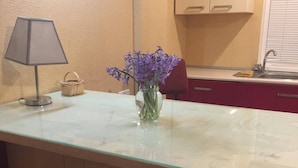 Une cuisine avec un plan de travail en marbre, un vase rempli de fleurs violettes, une lampe et un panier.